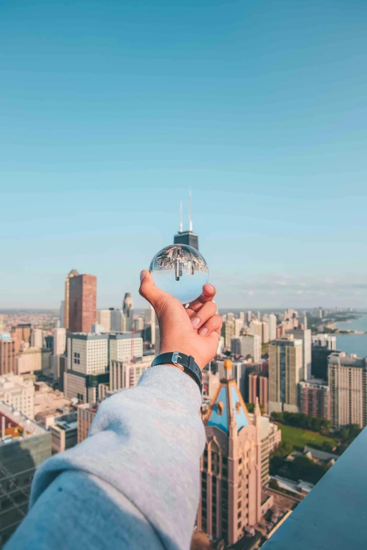 a person holding a crystal ball in front of a cityscape, by Jacob Burck, pexels contest winner, holding a postcard from chicago, sky - high view, instagram post, shot from roofline