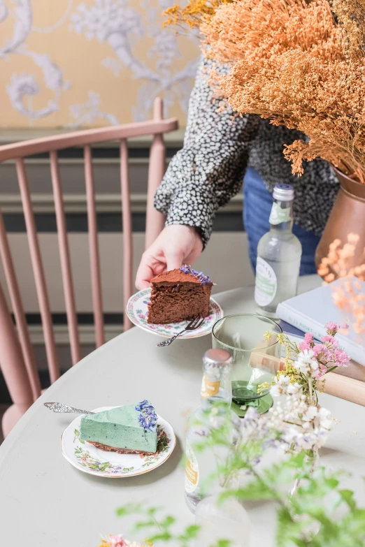 a woman sitting at a table with a piece of cake, by Lucette Barker, trending on unsplash, happening, herbs and flowers, nordic pastel colors, brown, high quality photo