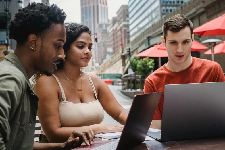 three people sitting at a table looking at a laptop, pexels contest winner, varying ethnicities, college students, background image, city views