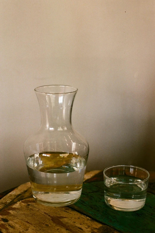 a pitcher sitting on top of a wooden table next to a glass of water, a still life, by Jan Rustem, unsplash, close up front view, portrait n - 9, jen yoon, glassware