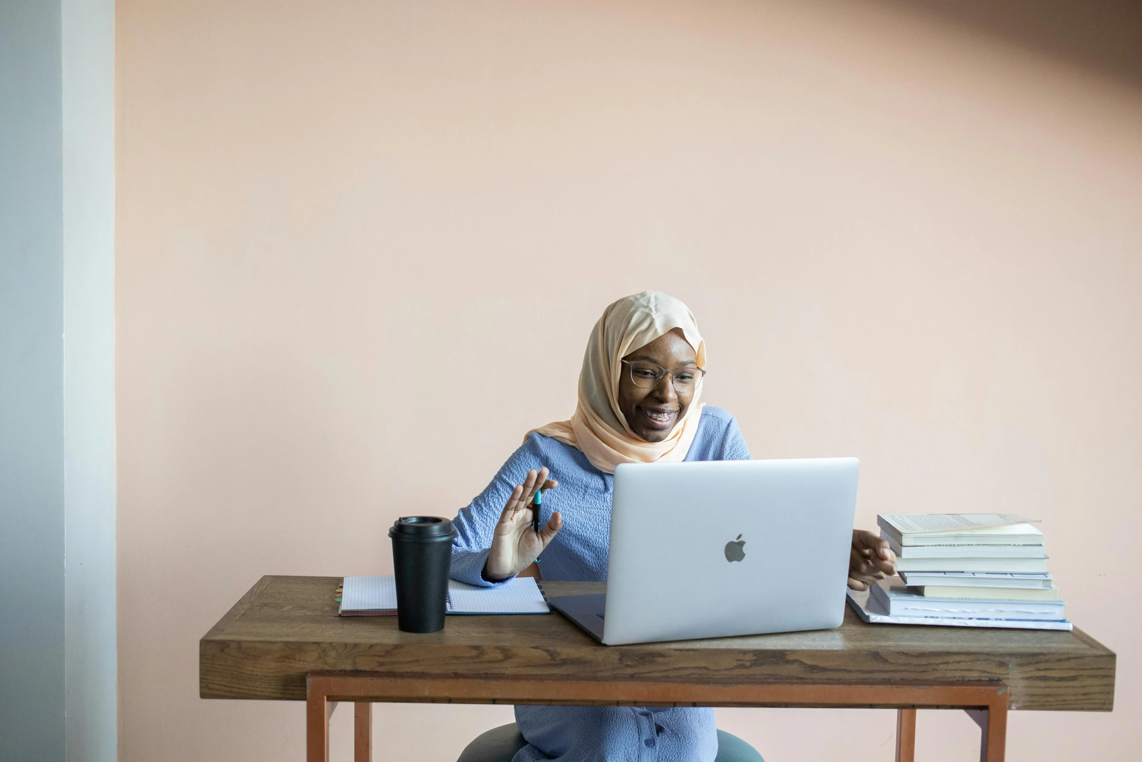 a woman sitting at a table with a laptop, by Arabella Rankin, pexels contest winner, hurufiyya, peach and goma style, excited, islamic, slightly minimal