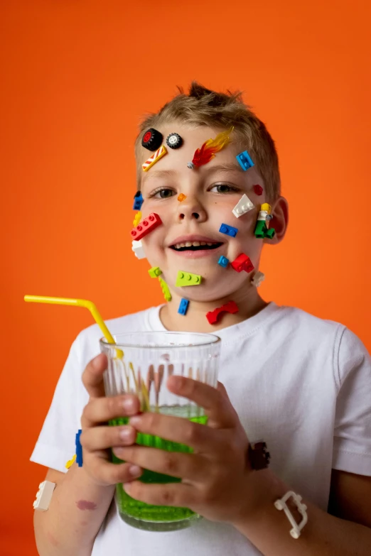 a young boy with sprinkles on his face holding a drink, inspired by Damien Hirst, pexels, plasticien, building blocks, machine parts embedded into face, fluorescent, with a straw