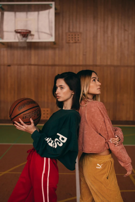 two women standing next to each other on a basketball court, by Matija Jama, trending on dribble, wearing a sweater, promo image, on a wooden table, dasha taran