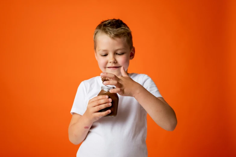 a young boy holding a jar of peanut butter, by Nick Fudge, pexels contest winner, in front of an orange background, chocolate sauce, manuka, fun pose