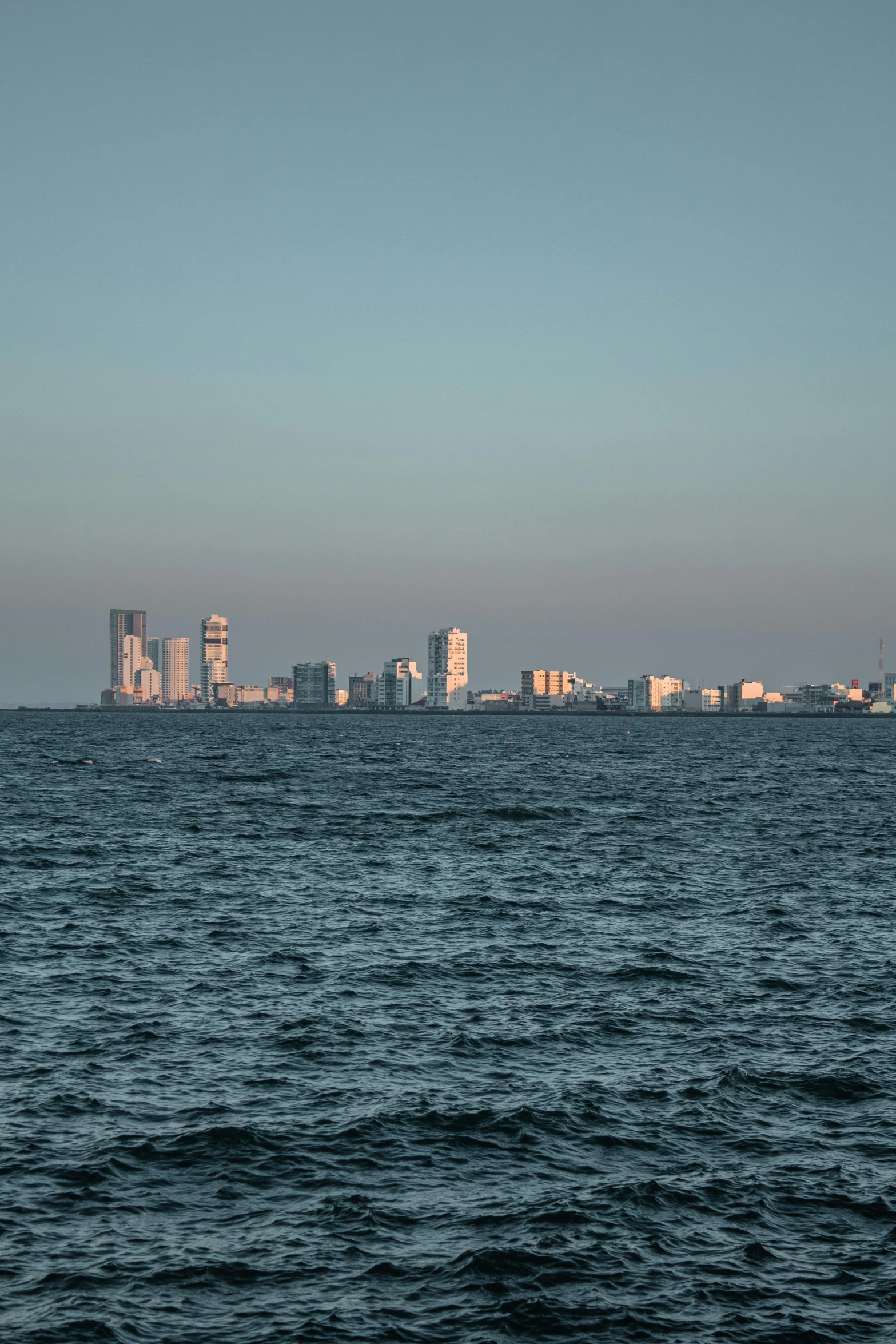 a large body of water with a city in the background, a picture, high-resolution photo, view from the sea, 2022 photograph, during golden hour