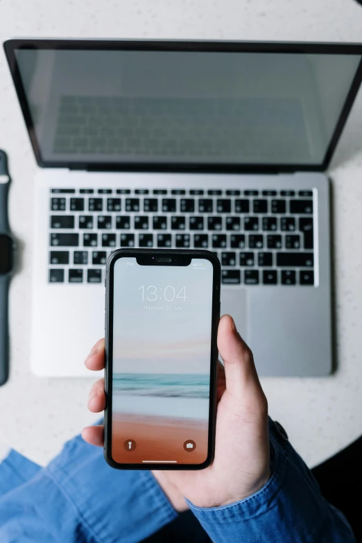 a person holding a phone in front of a laptop, by Carey Morris, trending on unsplash, iphone 13, low quality photo, modern minimalist f 2 0, computer setup