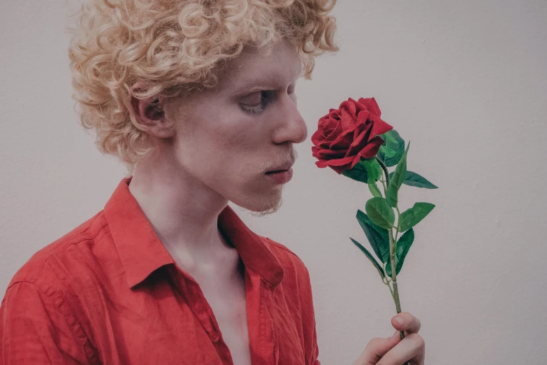 a close up of a person holding a flower, an album cover, inspired by Lasar Segall, tumblr, pale skin curly blond hair, holding a red rose, male model, nonbinary model