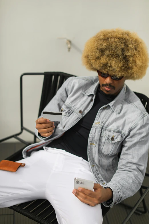 a man sitting in a chair with a cell phone, an album cover, inspired by Michael Gustavius Payne, pexels contest winner, afrofuturism, short blonde afro, tipping his fedora, typical cryptocurrency nerd, candid shot