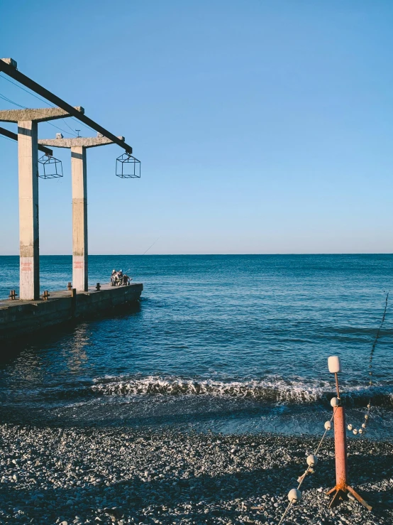 a man standing on top of a beach next to the ocean, boat dock, black sea, cables hanging, image from afar