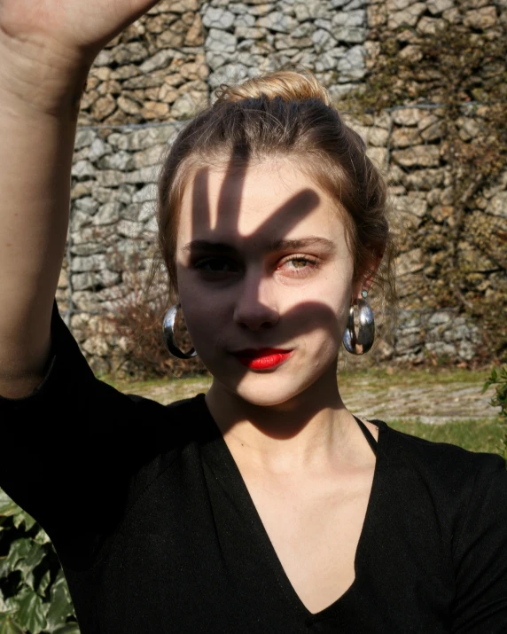 a woman posing for a picture in front of a stone wall, inspired by Taro Yamamoto, pexels contest winner, big shadows, red lipstick on face, photo of džesika devic, hands not visible