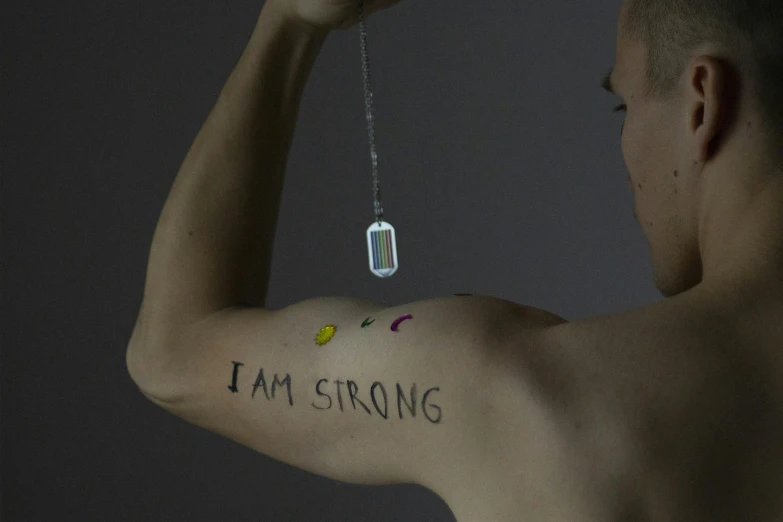 a man with a tattoo that says i am strong, by Siona Shimshi, conceptual art, dichroic prism, wearing several pendants, filmstill, wei wang
