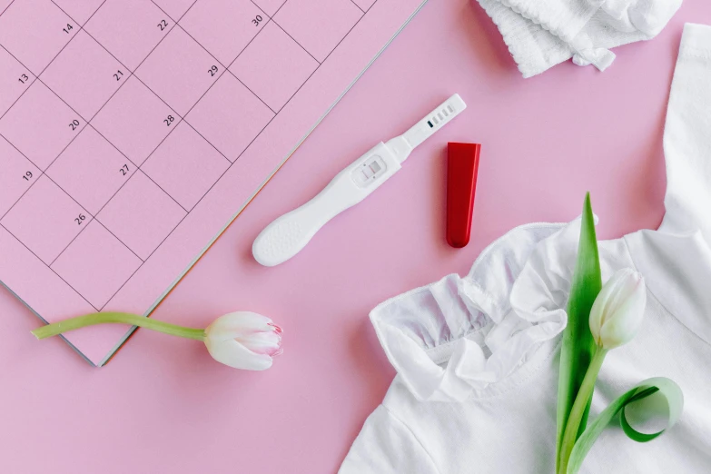 a pink calendar sitting on top of a table next to a flower, a picture, contracept, wearing white cloths, red color theme, with a sleek spoiler