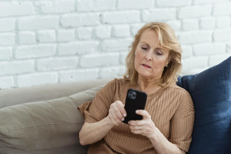 a woman sitting on a couch looking at her cell phone, pexels, happening, two old people, 😭🤮 💔