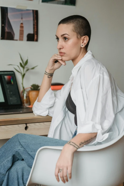 a woman sitting in a chair in front of a laptop, inspired by Elsa Bleda, trending on pexels, shaved hair, white shirt, outfit photo, thoughtful )