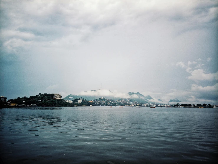 a large body of water with a mountain in the background, by Elsa Bleda, medium format, grey sky, distant city, lomography photo