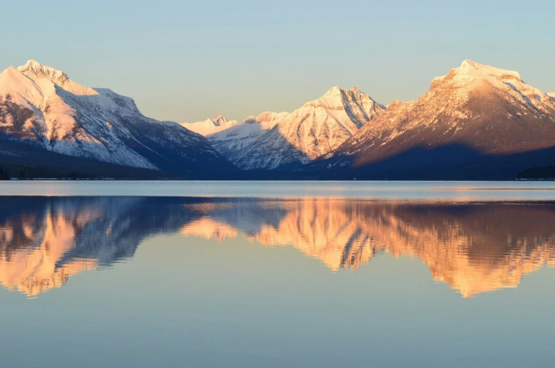 a large body of water with mountains in the background, by Winona Nelson, pexels contest winner, fan favorite, snow capped mountains, morning glow, clear reflection