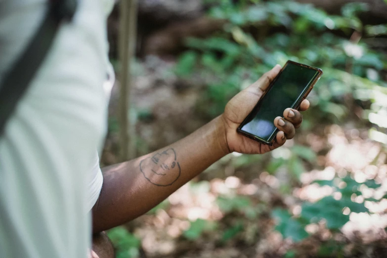 a person holding a cell phone in their hand, a tattoo, trending on pexels, brown skin like soil, forest soul, avatar image, ignant