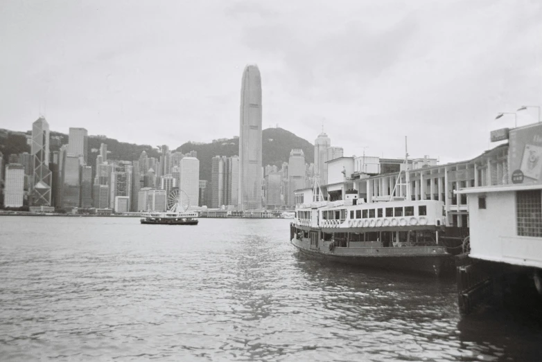 a black and white photo of a boat in the water, inspired by Thomas Struth, temporary art, city like hong kong, polariod, kings row in the background, vintage film photo