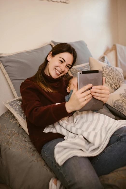 a woman sitting on a bed using a tablet computer, pexels contest winner, incoherents, with a kid, happy cozy feelings, grey, on a couch