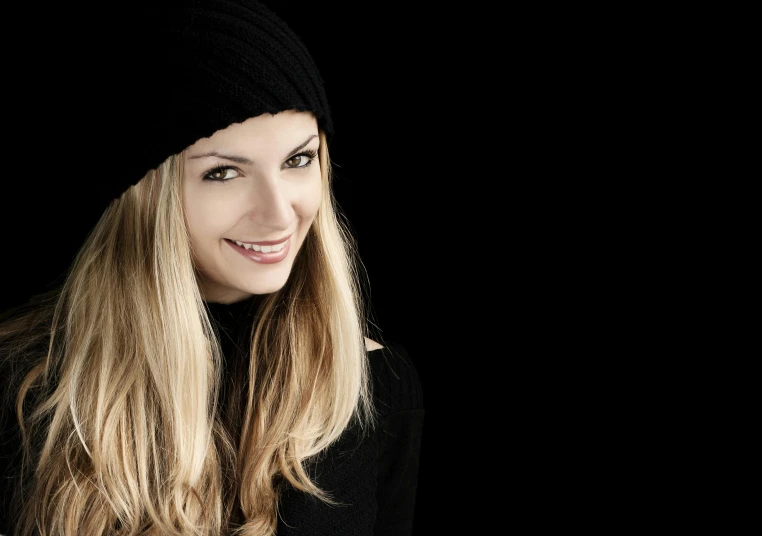 a woman with long blonde hair wearing a black hat, inspired by Ksenia Milicevic, shutterstock, black background, beanie, sweet smile, taken in the late 2010s