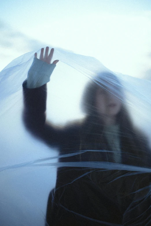 a blurry image of a woman holding an umbrella, an album cover, inspired by Anna Füssli, unsplash, conceptual art, draped in transparent cloth, in an igloo, hands shielding face, morning detail