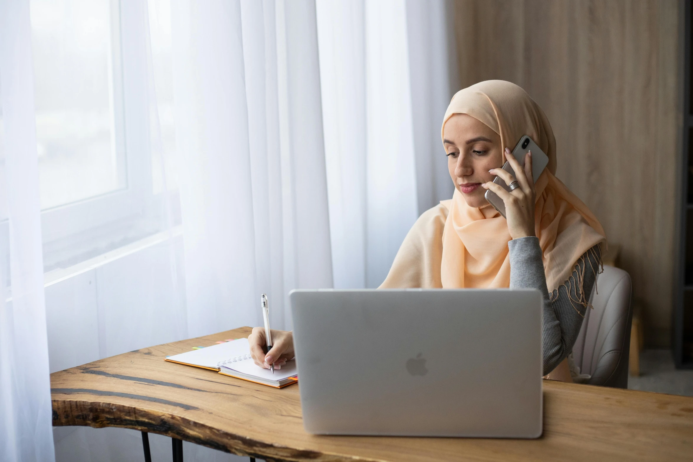 a woman sitting at a table talking on a cell phone, inspired by Maryam Hashemi, trending on pexels, hurufiyya, laptops, islamic, thumbnail, malaysian