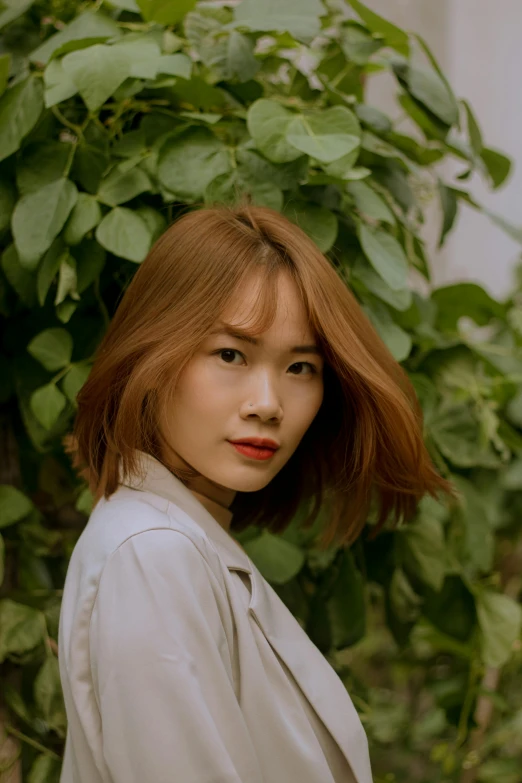 a woman standing in front of a tree, inspired by Ruth Jên, trending on pexels, photorealism, chestnut hair, vietnamese woman, short green bobcut, light-red lips