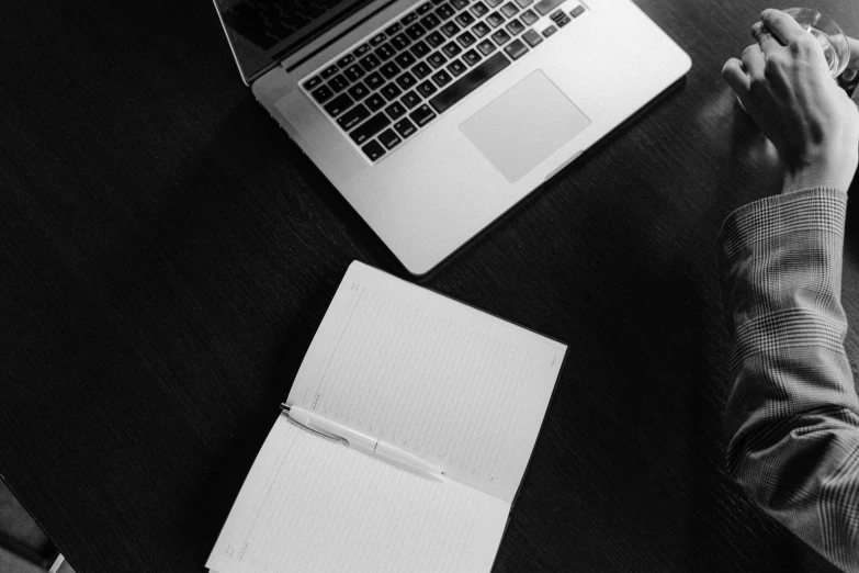 a man sitting at a table in front of a laptop computer, a black and white photo, by Daniel Gelon, pexels, lined paper, [ overhead view of a table ]!!, notebook, stacked image