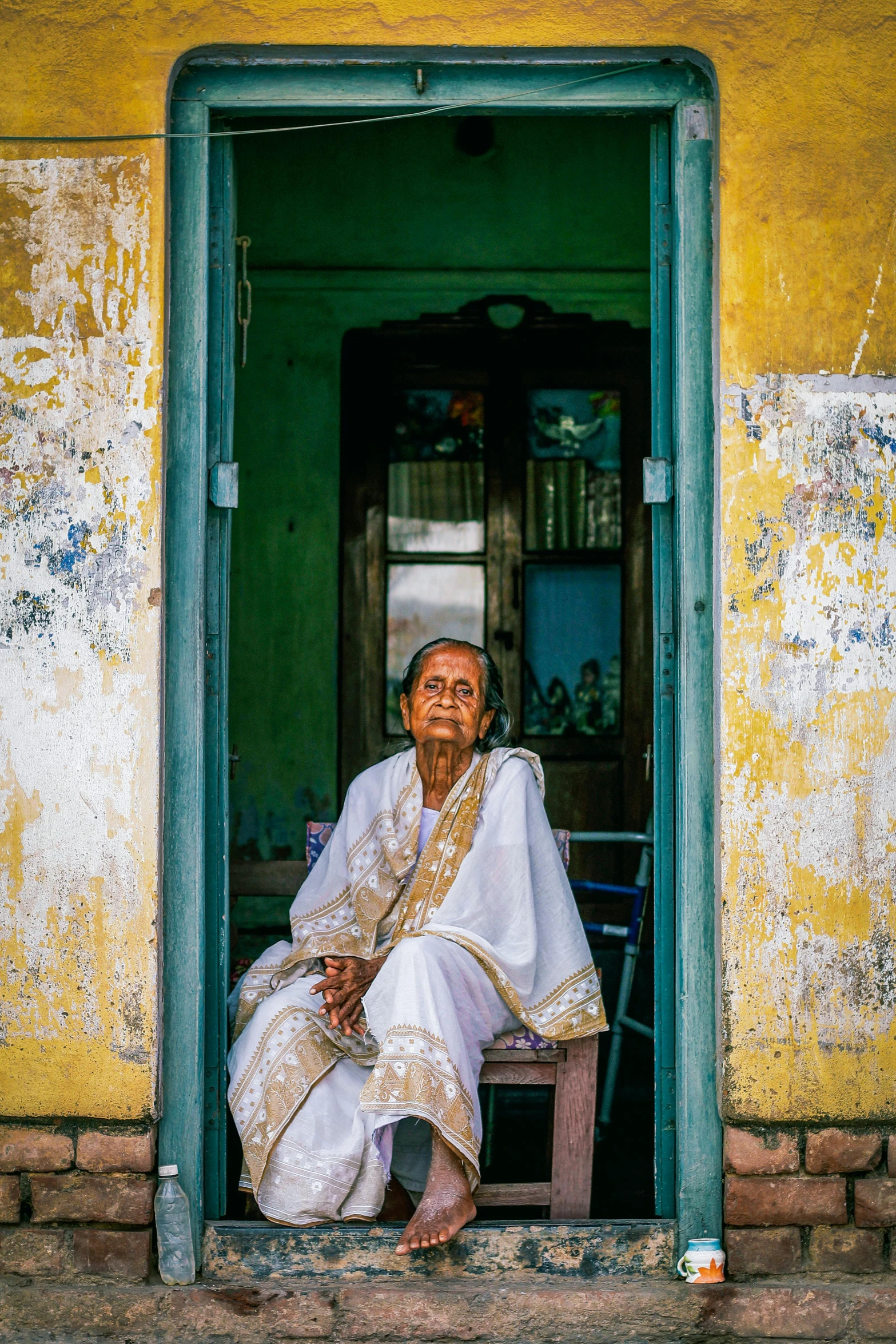 a woman sitting in a doorway of a building, a portrait, pexels contest winner, bengal school of art, an elderly, intense color, a beautiful woman in white, square