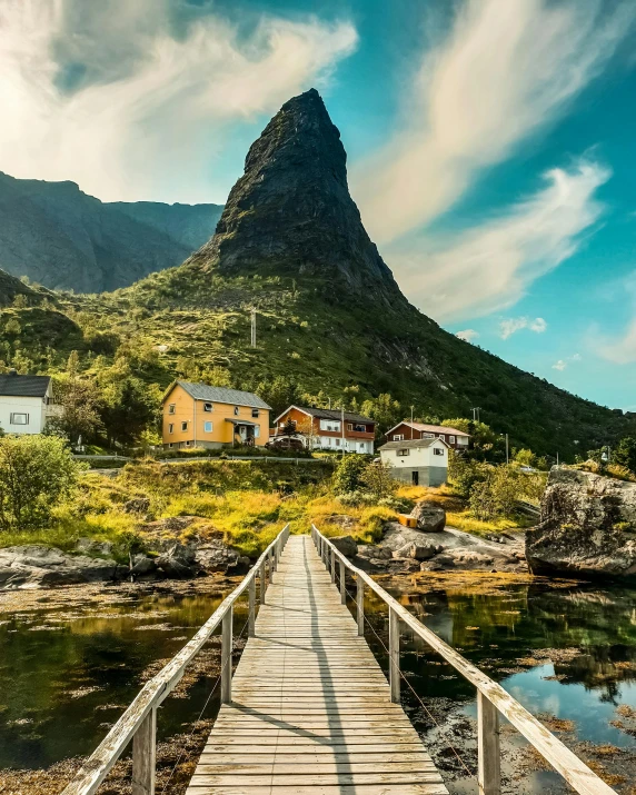 a wooden bridge over a body of water, by Anton Lehmden, pexels contest winner, norway mountains, behind a tiny village, thumbnail, conde nast traveler photo