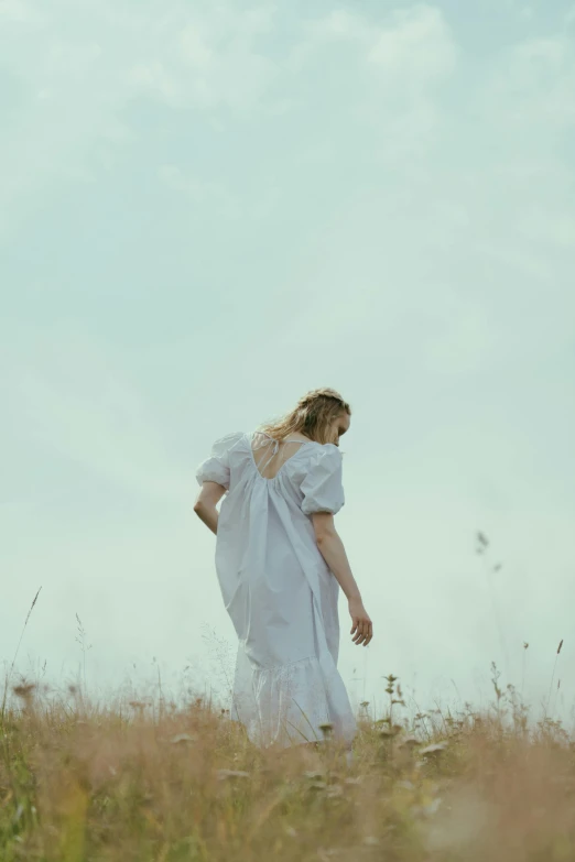 a woman in a white dress walking through a field, inspired by Elsa Bleda, pexels contest winner, happening, back turned, promo still, young southern woman, uniform off - white sky