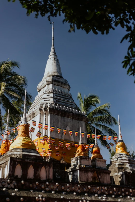 a large white and yellow building surrounded by palm trees, unsplash, renaissance, thai temple, flags, lead - covered spire, grey