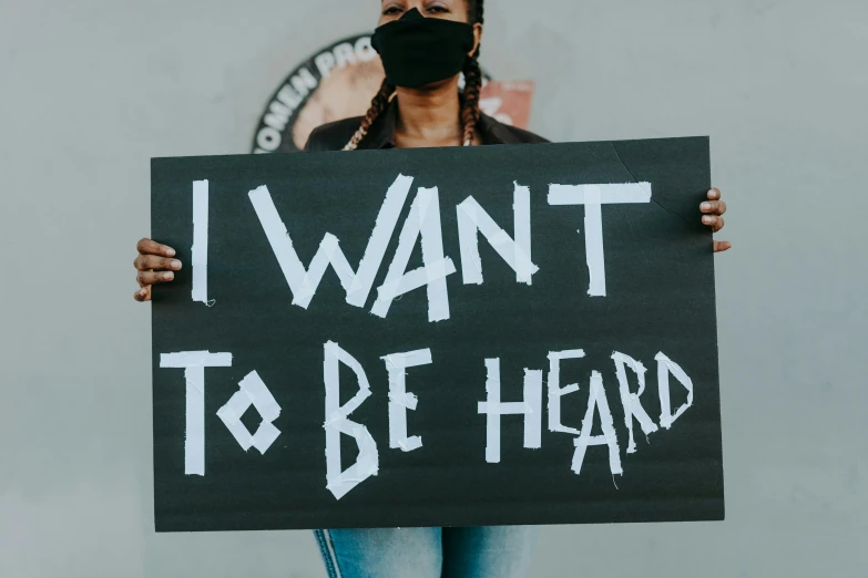 a woman holding a sign that says i want to be hard, by Julia Pishtar, trending on pexels, black arts movement, ears are listening, on a canva, that violence breeds violence, you wanted to