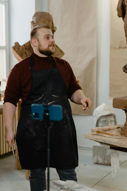 a man that is standing in front of a statue, arbeitsrat für kunst, wearing an apron, clay animation, kacper niepokolczycki, heavy looking