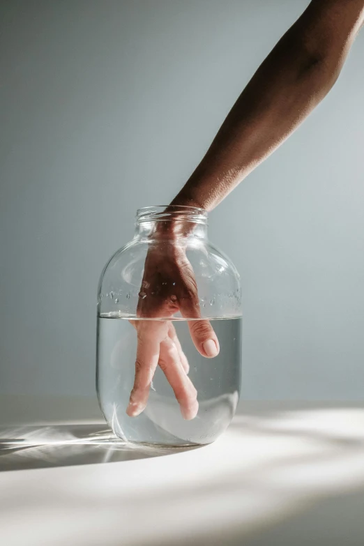a hand reaching into a glass jar filled with water, scaled arm, but minimalist, trending photo