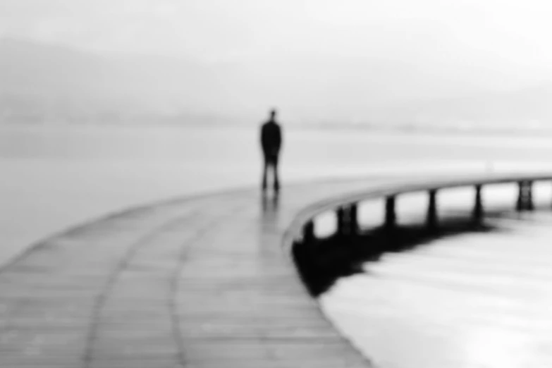 a black and white photo of a person walking on a pier, a picture, by Michalis Oikonomou, conceptual art, defocus, 'lone dark figure'!!, silhouette :7, sad men