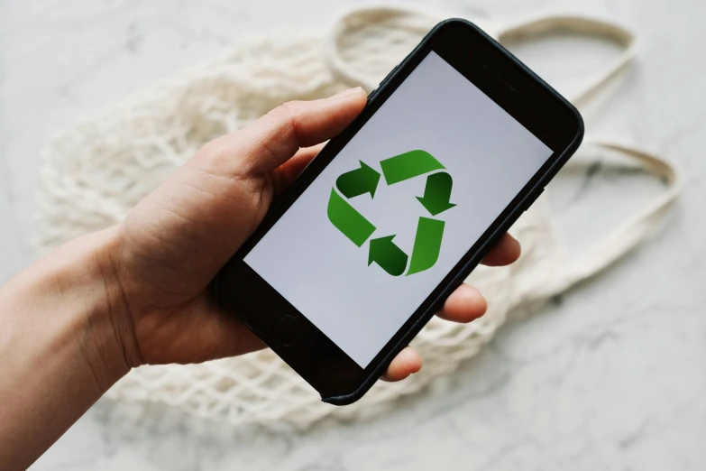 a person holding a cell phone with a recycle logo on the screen, trending on pexels, hurufiyya, essence, sustainable materials, minna sundberg, greens)