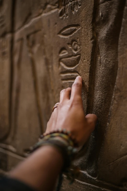 a person touching the side of a stone wall, egyptian art, trending on pexels, jewelry engraved in scarab, angkor thon, a wooden, ancient”