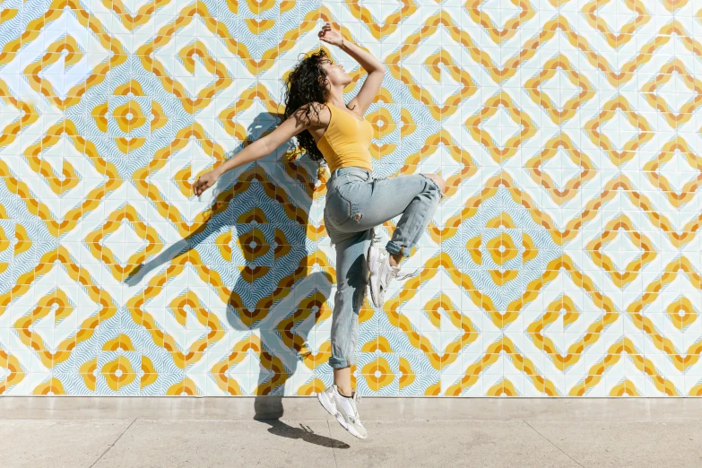 a woman standing in front of a colorful wall, trending on pexels, arabesque, jump pose, background image, tiled, wearing yellow croptop