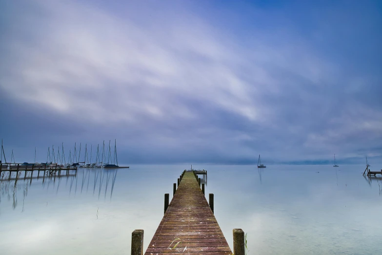 a dock in the middle of a body of water, by Peter Churcher, pexels contest winner, light blue mist, overcast dusk, sailboats in the water, new zealand