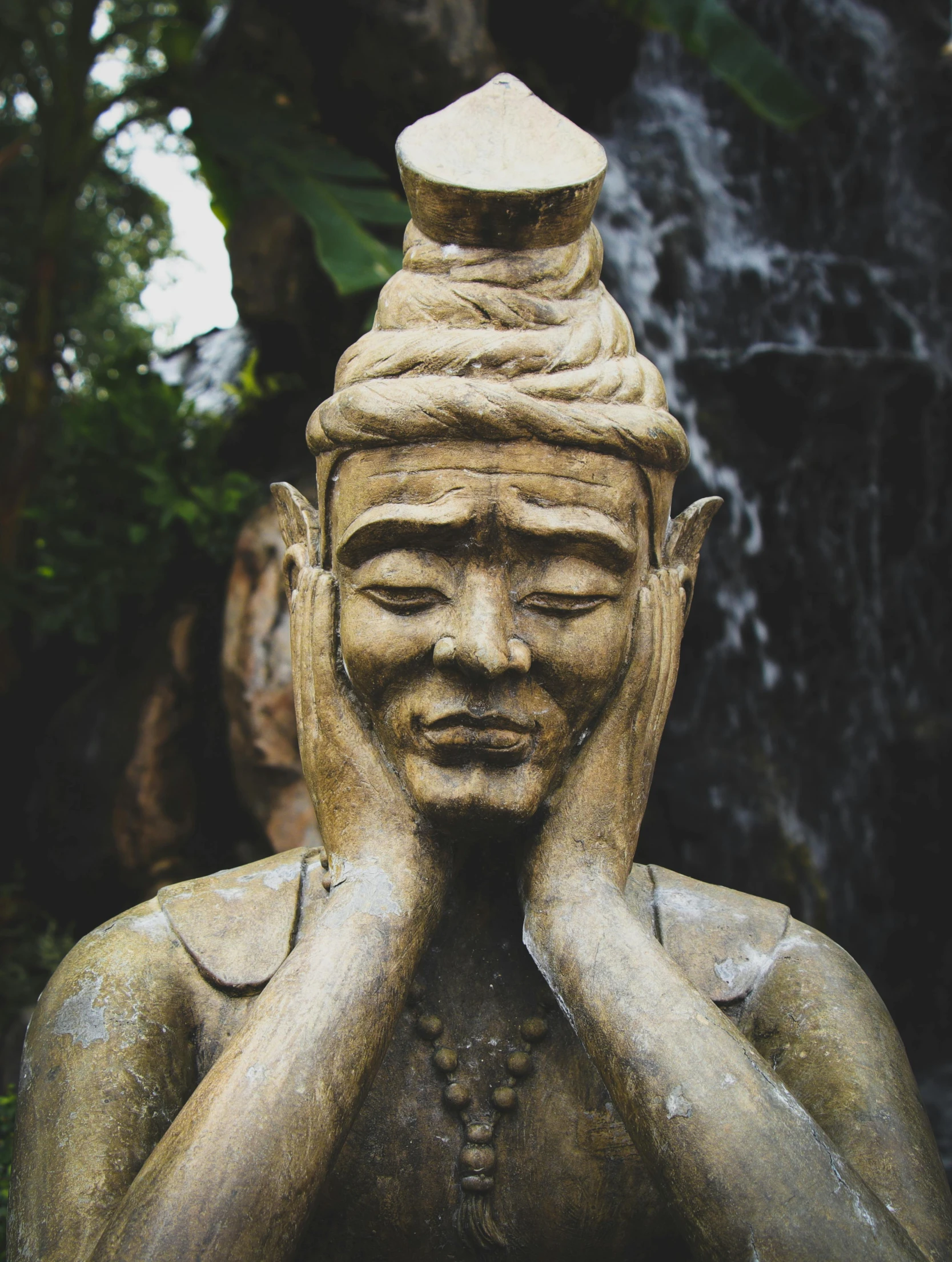 a statue sitting in front of a waterfall, wise forehead, eyes closed, south east asian with round face, channeling third eye energy