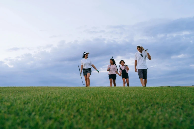 a group of people walking across a lush green field, wrx golf, happy family, tony taka, in the evening
