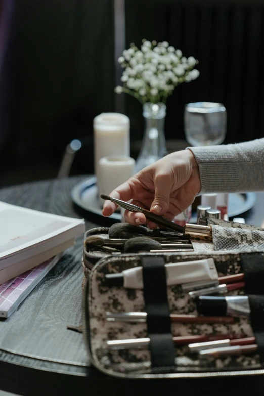 a woman sitting at a table with a purse full of makeup brushes, trending on pexels, holding books, cinematic photo, hands on counter, inspect in inventory image