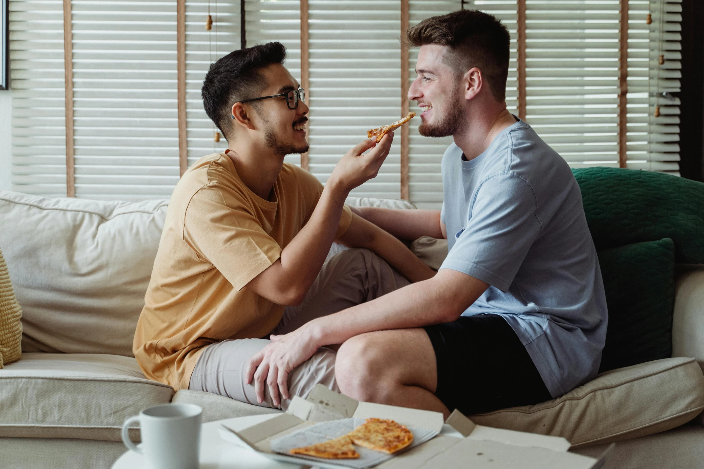 two men sitting on a couch eating pizza, trending on pexels, lesbians, on a hot australian day, profile pic, loveable guy