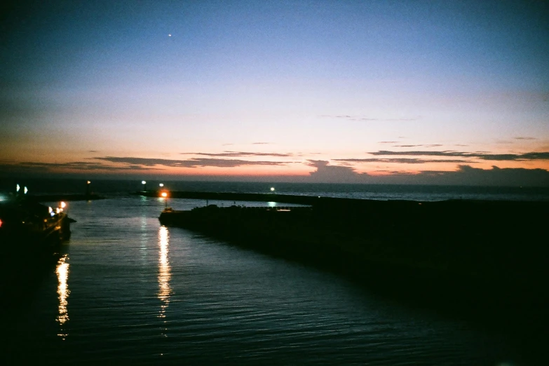 a couple of boats that are in the water, a polaroid photo, inspired by Elsa Bleda, unsplash, happening, city lights on the horizon, vsco film grain, near a jetty, humid evening