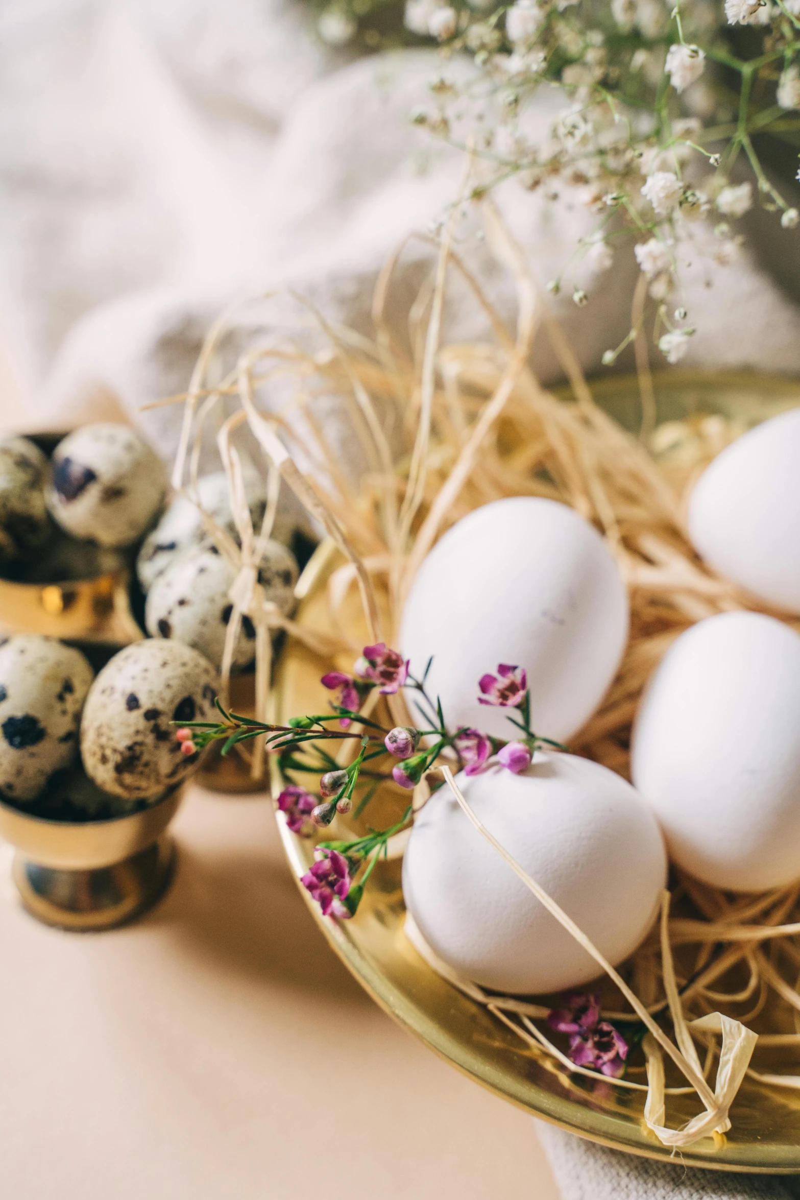 a bowl filled with eggs sitting on top of a table, a still life, by Adam Marczyński, trending on unsplash, renaissance, flower decorations, white with gold accents, hay, high quality product photo