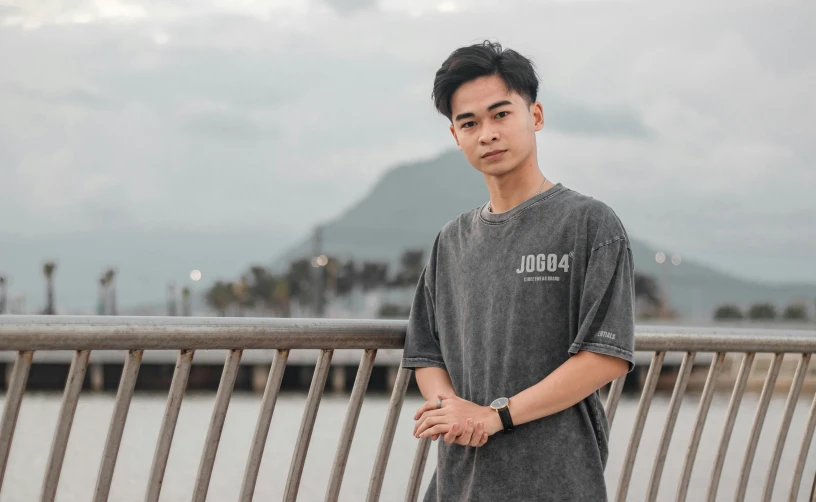 a man standing on a bridge next to a body of water, a picture, inspired by Jason Chan, pexels contest winner, portrait of jossi of blackpink, wearing a t-shirt, discord profile picture, student
