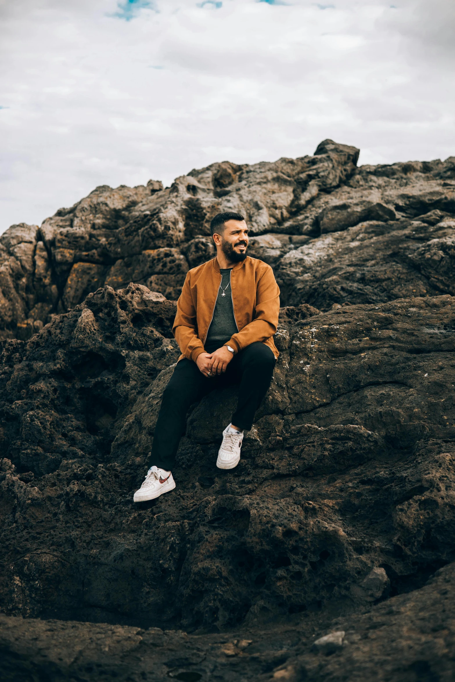 a man sitting on a rock on a cloudy day, an album cover, pexels contest winner, a portrait of rahul kohli, subreddit / r / whale, aboriginal australian hipster, caramel. rugged