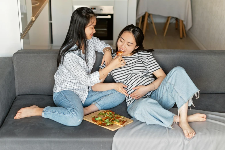 two women sitting on a couch eating pizza, by Julia Pishtar, pexels contest winner, pregnant, she is korean, holding each other, profile image