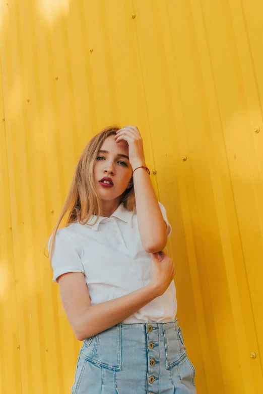 a woman standing in front of a yellow wall, inspired by Elsa Bleda, trending on pexels, portrait of white teenage girl, wearing polo shirt, promotional image, colored photo